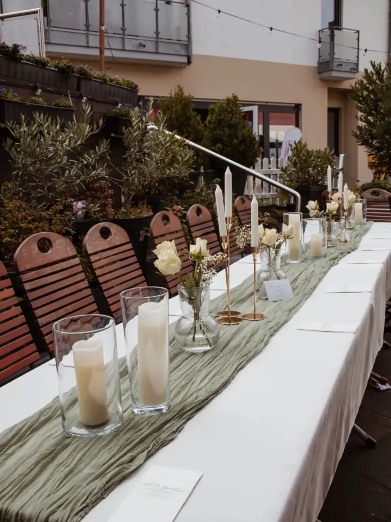Elegante Hochzeitstafel mit salbeigrünem Läufer, Kerzen und weißen Blumen – Deko von Fam.Deko