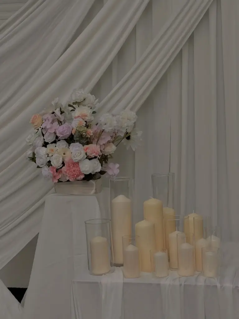 Blumengesteck in Rosé und Weiß mit Stumpenkerzen vor Stoffdrapierung – Fam.Deko